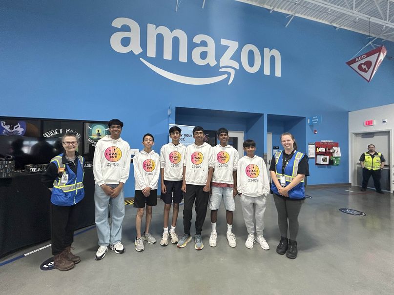 The team standing with two staff members under the Amazon sign inside a fulfillment center.