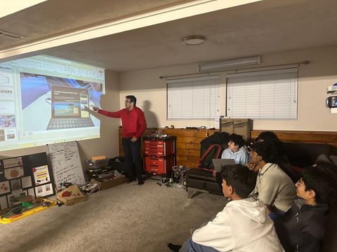 An engineer presenting slides to the seated team in their build space.
