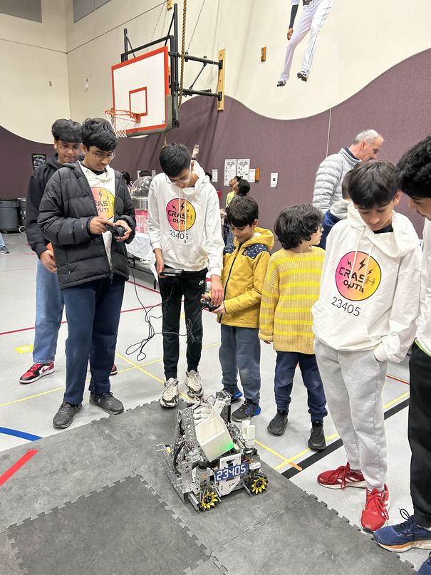 Team members in Crash Out hoodies showing their robot to a group of young children at a school science fair booth.